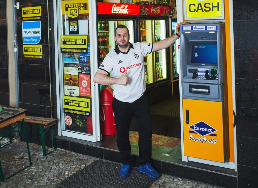Abbildung - Spätkaufbetreiber Burcak neben dem Euronet-Geldautomaten an seinem Geschäft